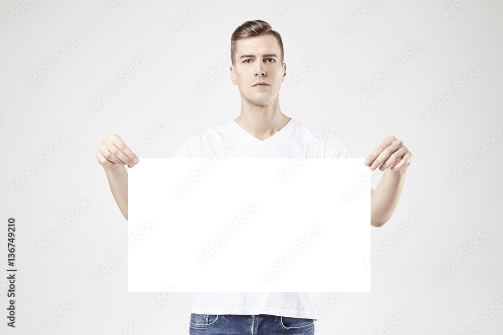 Handsome man model standing with blank big poster or sheet in hands, isolated on white background, wearing jeans and t-shirt Handsome man model standing with blank big poster or sheet in hands, isolated on white background, wearing jeans and t-shirt