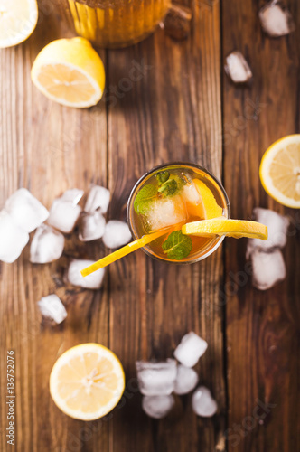 Lemon ice tea on brown wooden table with lemons around. Iced tea with lemon slices and mint on rustic background