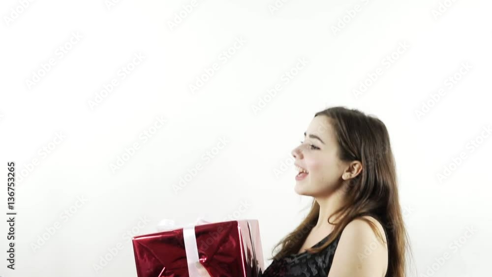 Pretty cheerful girl throw up a decorated red box, slow motion shot. Young woman in black shirt have fun at isoated white background, childlike enjoy her birthday gift. Merry and sincere emotions mood Pretty cheerful girl throw up a decorated red box, slow motion shot. Young woman in black shirt have fun at isoated white background, childlike enjoy her birthday gift. Merry and sincere emotions mood
