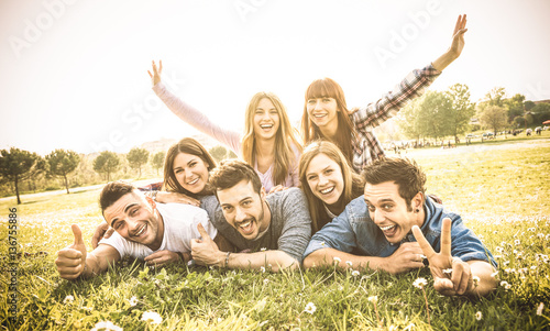 Friends group having fun together with self portrait on grass meadow - Friendship youth concept with young happy people at picnic camping outdoor - Warm vintage filter with backlight contrast sunshine