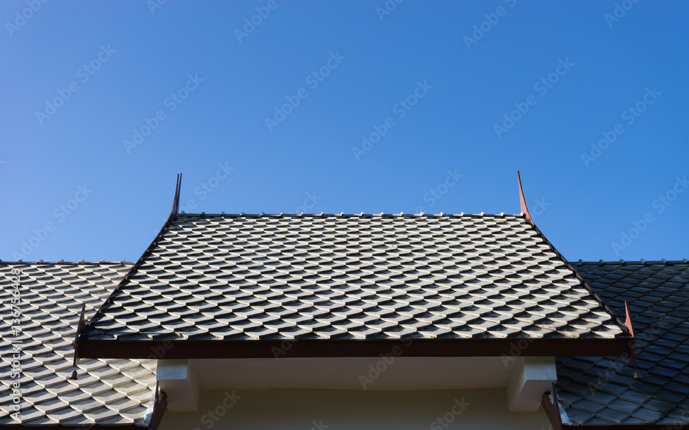 Thai style roof of buddhist temple with blue sky background