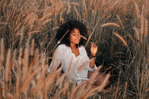 attractive young african american woman sitting on field at sunset