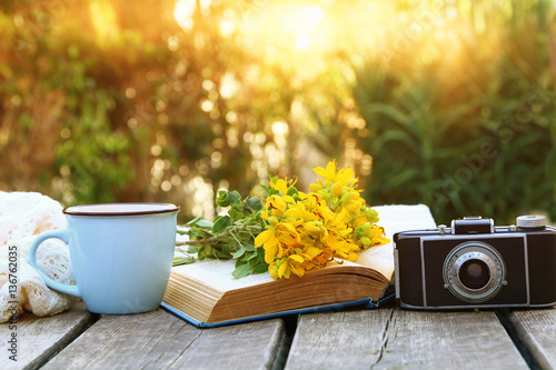 Fotografie old book, vintage photo camera next to field flowers