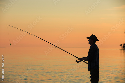 Silhouette of a fisherman with spinning at sunset