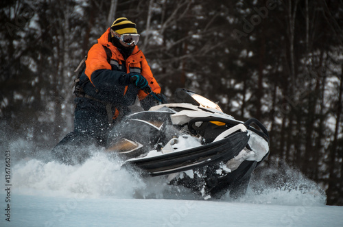 Boy athlete performs professional figure on a snowmobile in the winter forest