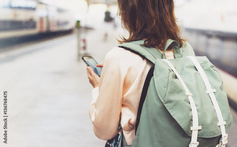 Enjoying travel. Young pretty woman waiting on the station platform with backpack on background electric train using smartphone. Tourist texting message and plan route of railway, railroad transport Enjoying travel. Young pretty woman waiting on the station platform with backpack on background electric train using smartphone. Tourist texting message and plan route of railway, railroad transport