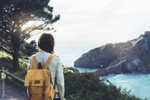 Hipster young girl with backpack enjoying sunset on seascape on peak mountain. Tourist traveler on background valley landscape view mockup. Hiker looking ocean in trip holiday in basque island