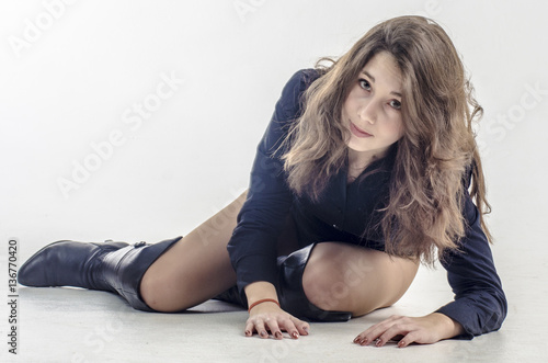 Young girl with curly hair sits gracefully coquettish in a dark shirt and high boots with heels 