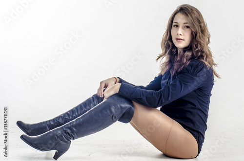 Fotografie Young girl with curly hair sits gracefully coquettish in a dark shirt and high b