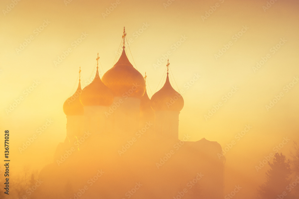 Golden domes in fog in sunlight as background. Winter frosty misty morning. Church in fog in background of rising sun.