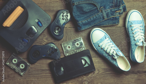 Back in the 90s. Shoes, audio tapes, video tapes, game console, jeans. Top view. Flat lat.