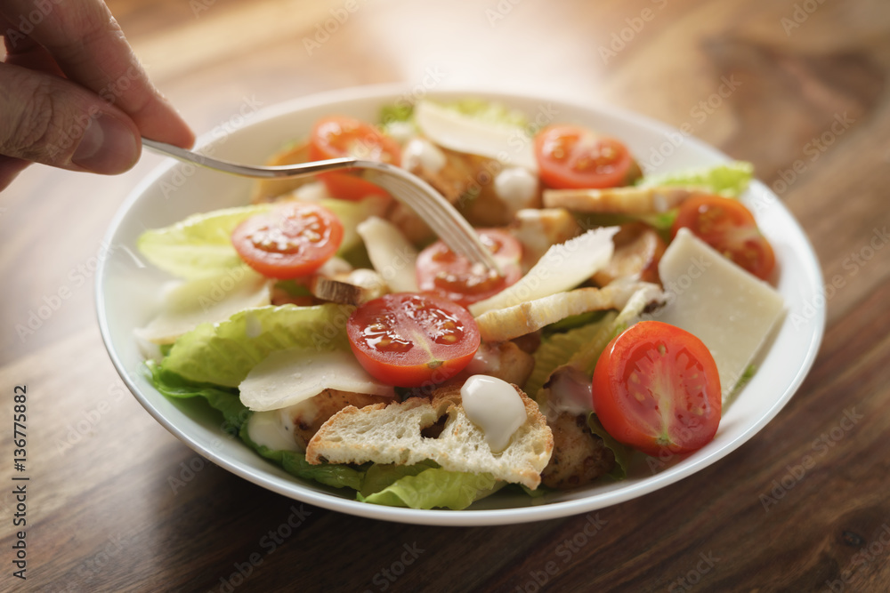 eating caesar salad with chicken and cherry tomatoes on wood table, shallow depth of field eating caesar salad with chicken and cherry tomatoes on wood table, shallow depth of field