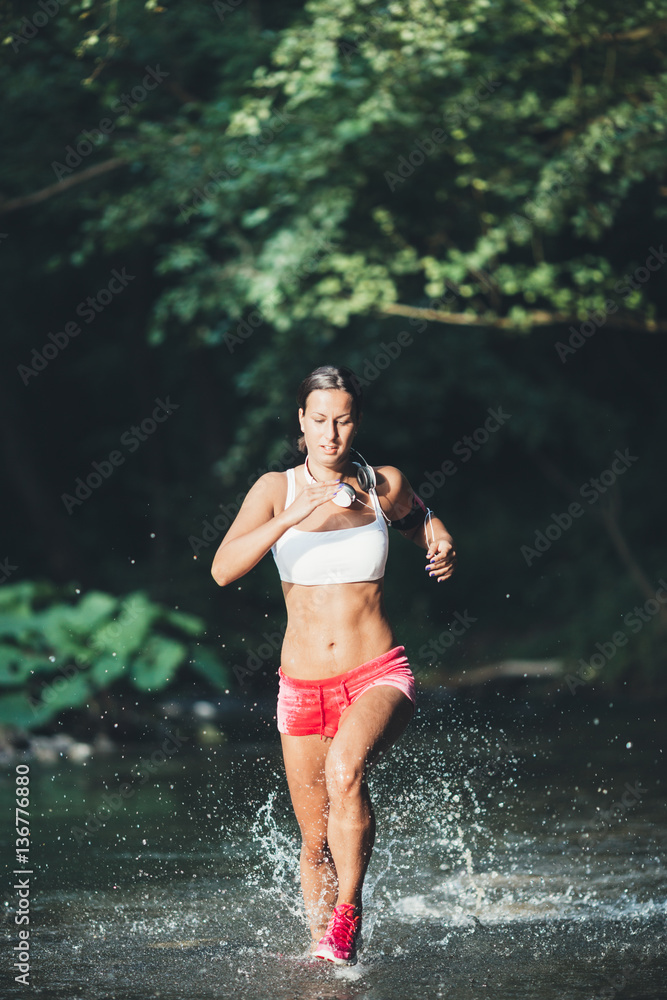 Fototapeta premium Attractive young woman running through river water. Hard training and sport theme.