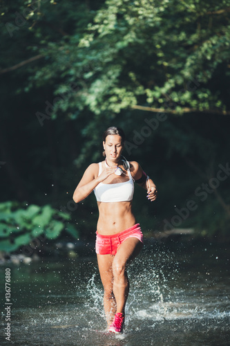 Attractive young woman running through river water. Hard training and sport theme.