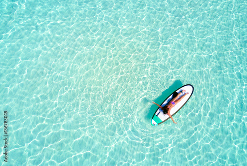 Frau auf Surfbrett paddelt über das türkise Wasser der Malediven