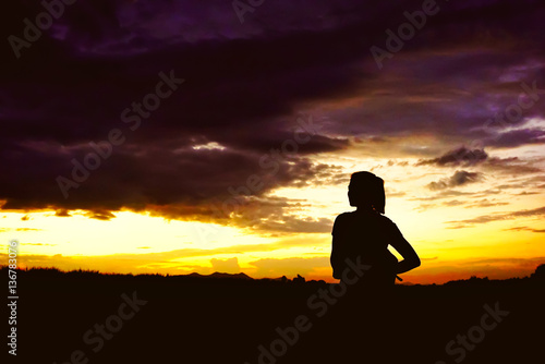 woman silhouette standing in front of a sun setting sky
