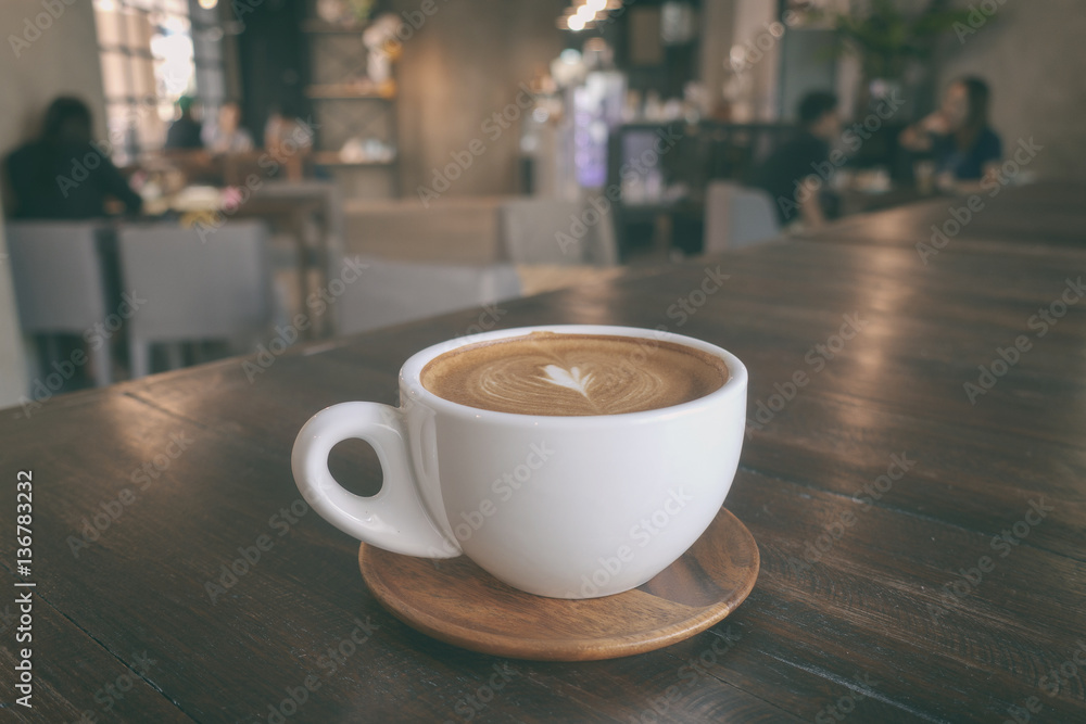 A cup of coffee latte on wooden table in warm cafeteria A cup of coffee latte on wooden table in warm cafeteria