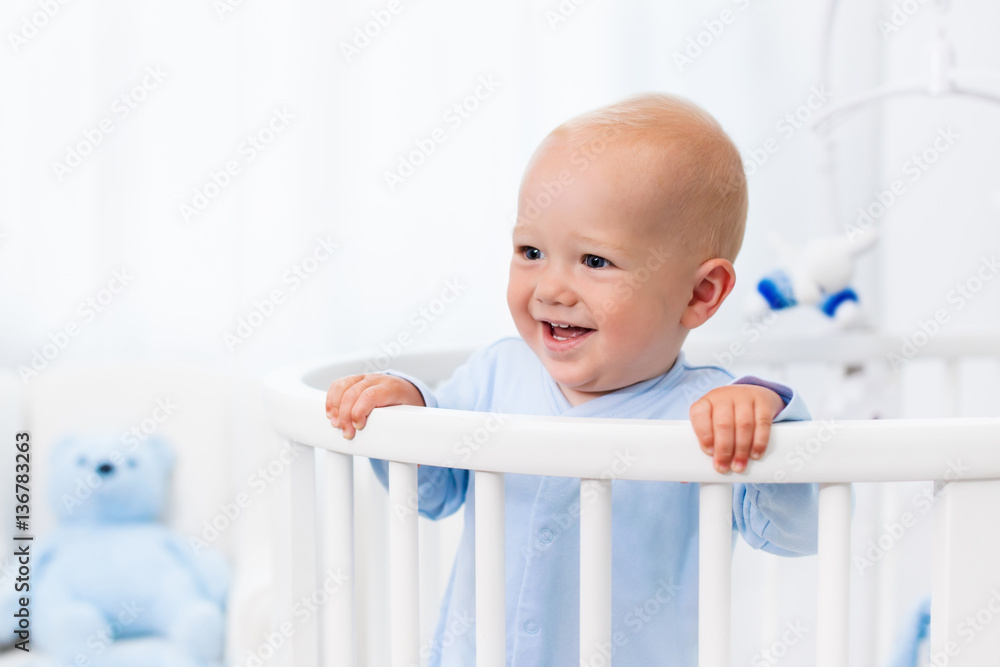 Baby boy standing in bed in white nursery Baby boy standing in bed in white nursery