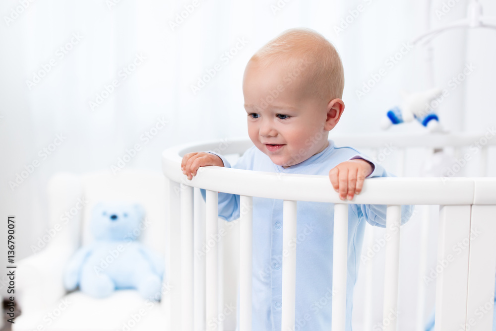 Baby boy standing in bed in white nursery Baby boy standing in bed in white nursery