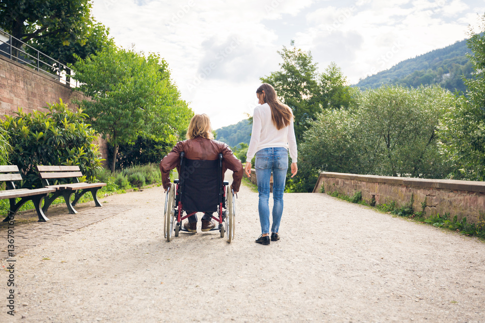 Young Couple In Wheelchair Strolling In The Park Young Couple In Wheelchair Strolling In The Park