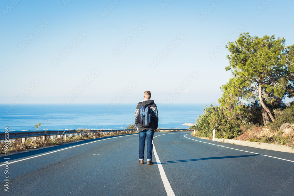 Young man with a backpack walks alone on a road. Travelling concept