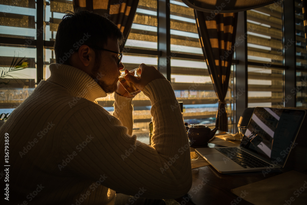 man in sweater working on laptop in caffe on sunset