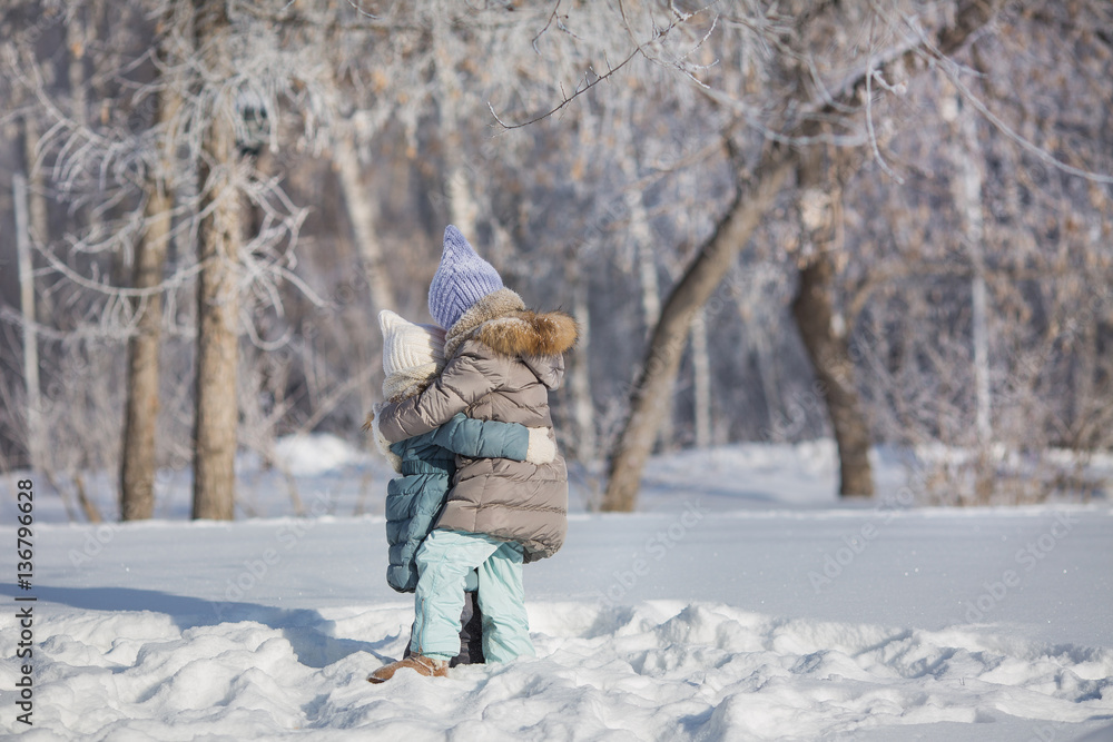Two little sisters hug each other in snow in winter