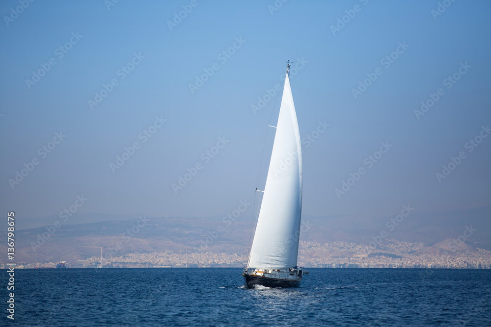 Sailing yacht with white sails in the sea near coast.