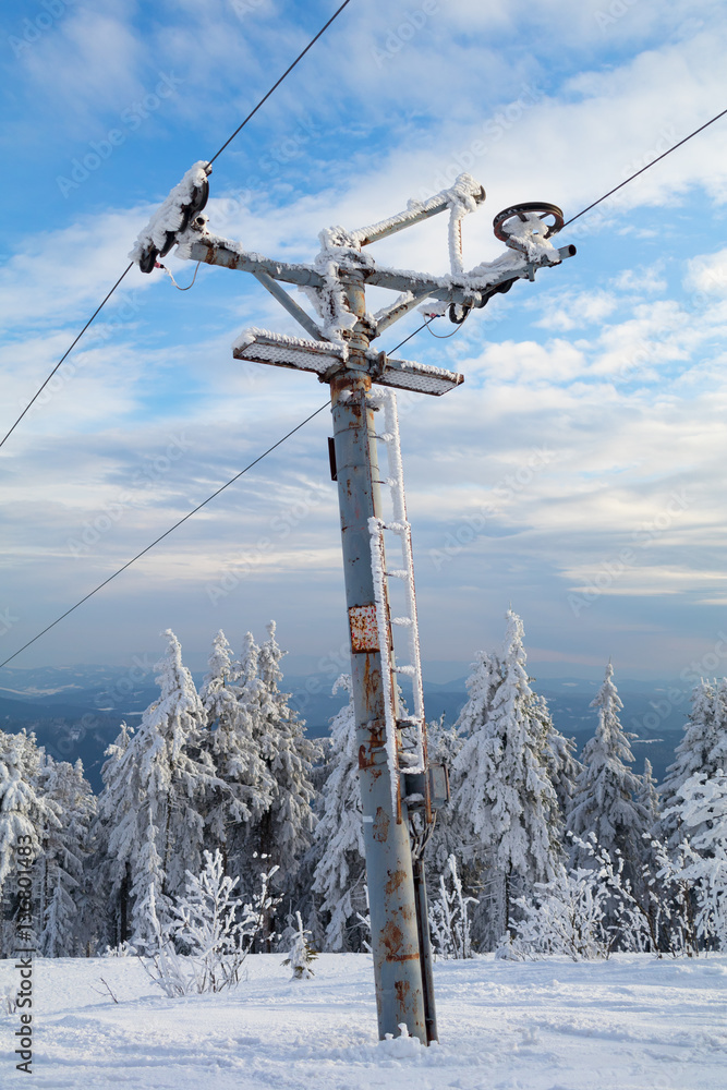 Old and rusty pole of ski tow - device for transportation in ski resort. Mechanism is surrounded by winter nature