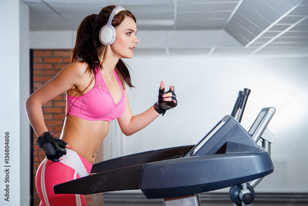 Fototapeta premium Fit girl with earphones running on treadmill in sports club