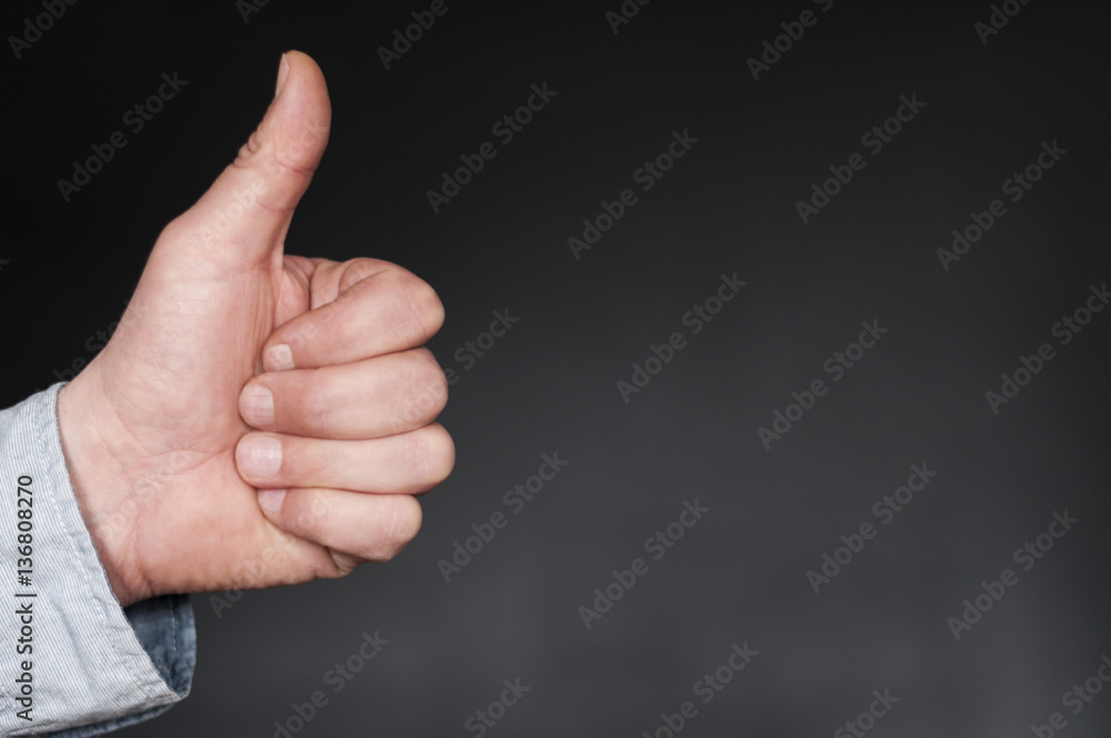 Hand mit Daumen nach oben / Positive Emotion, Hand mit Daumen hoch vor dunklem Hintergrund mit Textfreiraum. Hand mit Daumen nach oben / Positive Emotion, Hand mit Daumen hoch vor dunklem Hintergrund mit Textfreiraum.