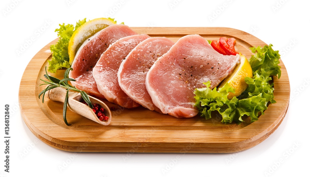 Raw pork chops on cutting board and vegetables Raw pork chops on cutting board and vegetables