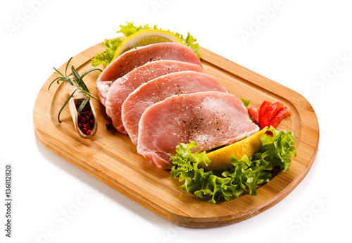 Raw pork chops on cutting board and vegetables 