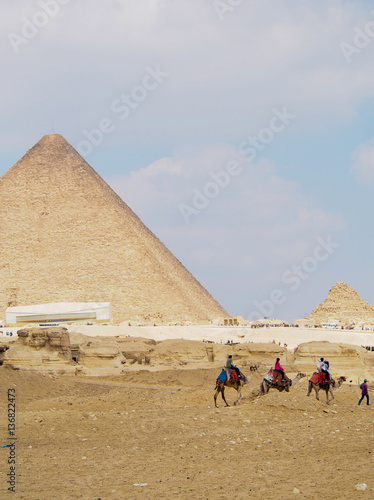 A row of camels bearing tourists walk past the great pyramids of Giza in Cairo Egypt.