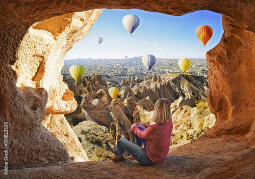 Woman watching like colorful hot air balloons flying over the valley at Cappadocia, Turkey. Volcanic mountains in Goreme national park