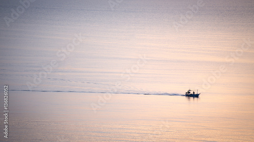 silhouette sunrise of minimal fishery boat sail on calm sea