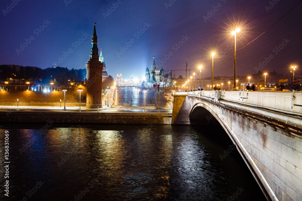 Obraz premium Night city view of Moscow Kremlin, Basil's Descent, embankment and steret lights at winter snowfall from Bolshoy Moskvoretsky Bridge in Moscow, Russia.