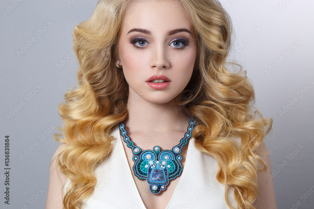 Beauty portrait of a beautiful young blonde woman in necklace isolated on gray background.