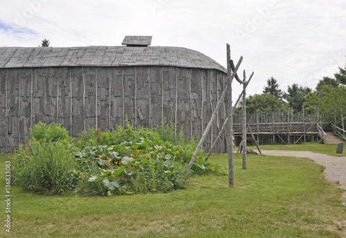 partial view of a historic native wooden longhouse with wooden palisade barricade in the background photo