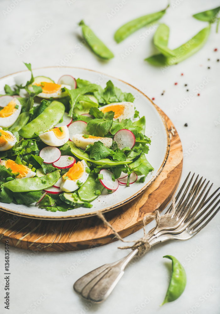 Healthy spring green salad with radish, boiled egg, arugula, green pea and mint in white plate on olive tree wood board over grey background, selective focus, vertical composition Healthy spring green salad with radish, boiled egg, arugula, green pea and mint in white plate on olive tree wood board over grey background, selective focus, vertical composition