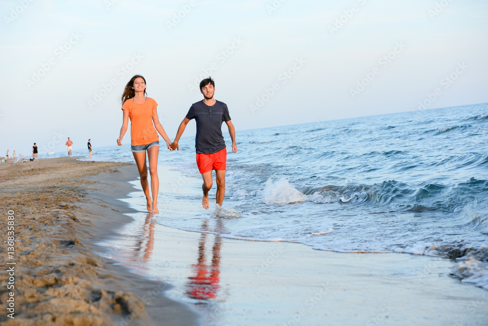 romantic young couple walking barefoot together in sand along the beach of mediterranean sea at sunset