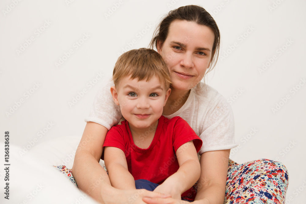 mother with little son dressed in pajamas are relaxing and playing in the bed at the weekend together, lazy morning. mother with little son dressed in pajamas are relaxing and playing in the bed at the weekend together, lazy morning.
