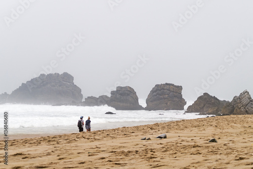 Young couple walk on foot along the shore of the ocean.