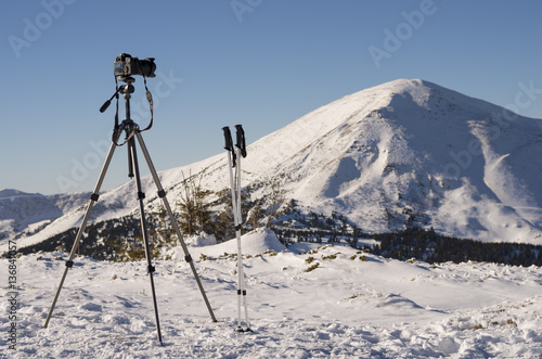 A camera on the tripod shoots the peak of mountain Petros on winter sunny day; Equipment for a photographer traveling in the mountains