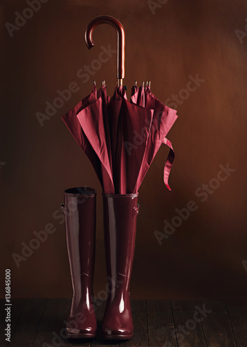 Photo in low key. Rubber boots and umbrella burgundy color on a