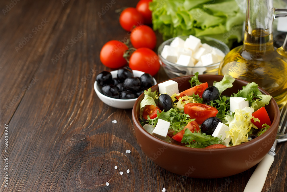 Tasty greek salad with feta, olives and tomatoes in a bowl on wooden background.