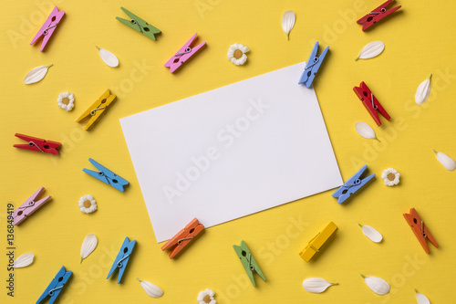 Spring or summer background with frame space for text: blank stationary template / invitation mockup, chamomiles and petals, many bright multicolored clothespins. Top view. Flat lay.