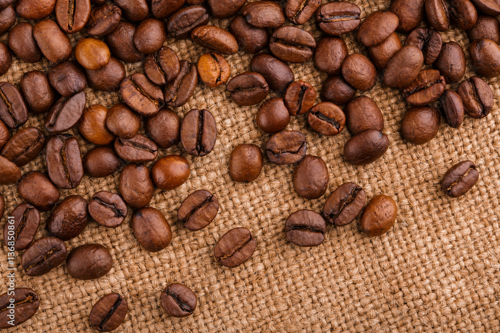 Fototapeta premium coffee beans on burlap background. roasted coffee beans isolated in white background. Roasted coffee beans background close up. Coffee beans pile from top on white background with copy space for text