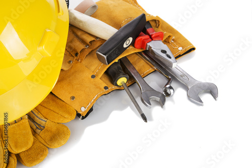 A yellow contractors hard hat on work gloves and tools. Horizontal format over white with reflection.