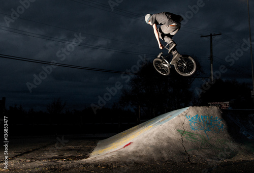 Man performing stunt on bike in skate park at night 